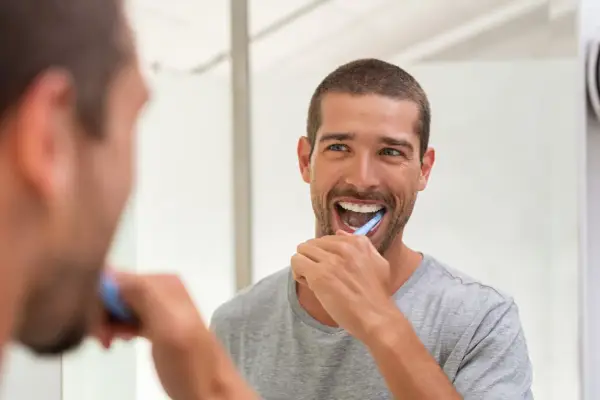 Uomo sorridente si lava i denti davanti allo specchio, un gesto quotidiano per la prevenzione odontoiatrica.