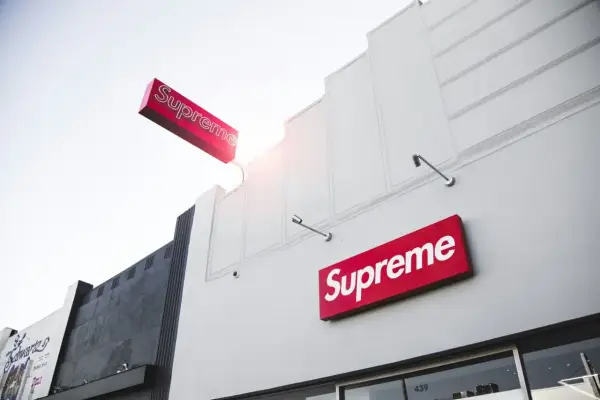 Znak Supreme na białej fasadzie budynku. Supreme to marka znana z limitowanych kolekcji streetwear.