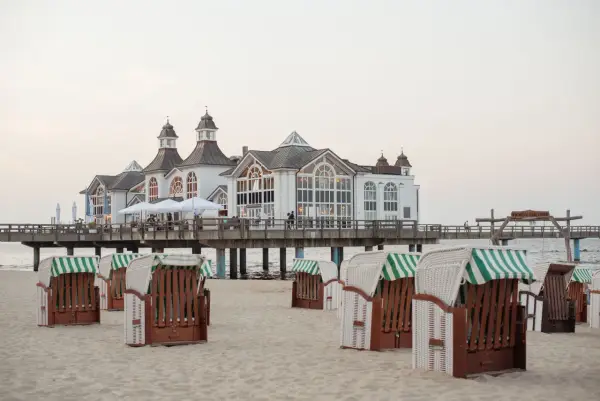 Plaża na wyspie Rugia z charakterystycznymi koszami plażowymi i molo prowadzącym do białego pawilonu.