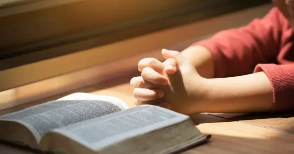 Dziecko z złożonymi dłońmi nad otwartą Biblią. To obraz modlitwy za córkę, pełen nadziei i wiary.