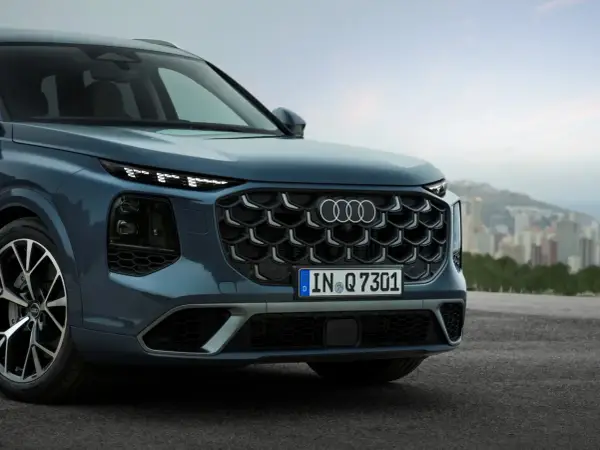Przód eleganckiego Audi Q7 3.0 TDI w kolorze granatowym, z charakterystycznym grillem i światłami LED, na tle miejskiego krajobrazu.