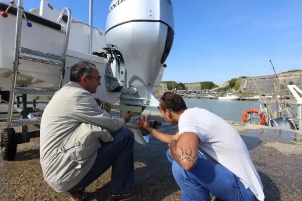 Deux hommes vérifient le montage moteur hors bord sur tableau arrière d'un bateau, près d'un port.