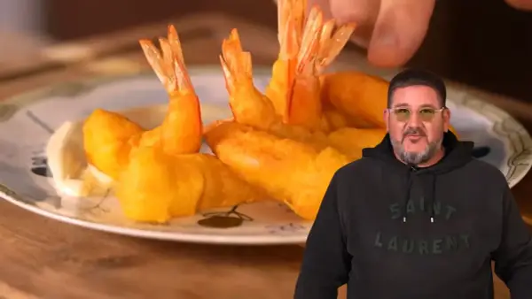 Un hombre sonriente muestra un plato de gambas a la gabardina doradas y crujientes, listas para disfrutar.