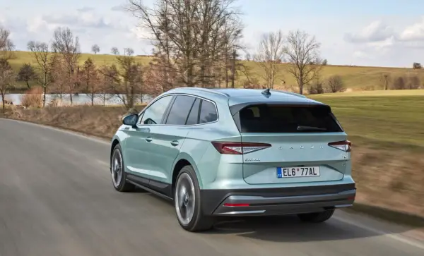 Jasnozielony Skoda Enyaq jedzie po wiejskiej drodze, otoczony wiosennym krajobrazem z drzewami i zielonymi polami.