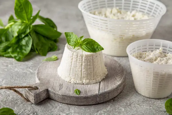 Świeża ricotta z bazylią, która zachęca do odkrycia, jak smakuje ricotta. Delikatny ser w koszyczkach i na desce.