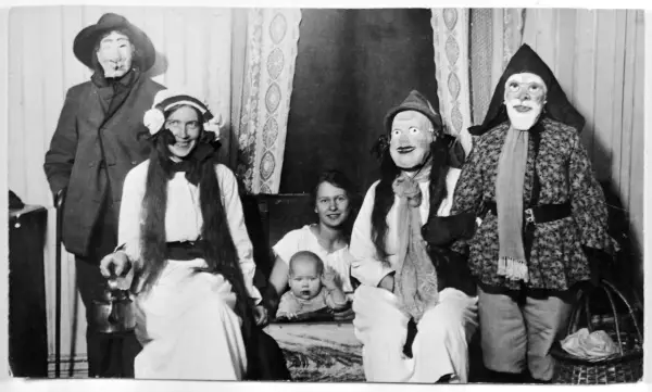 En familj klädd i masker och dräkter, kanske en del av julens historia, poserar för ett fotografi. En bebis sitter i förgrunden.