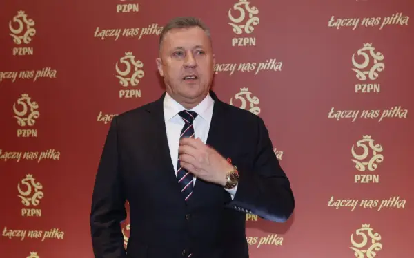 Prezes PZPN w garniturze, poprawiający krawat. Tło ozdobione logotypami PZPN i hasłem "Łączy nas piłka".