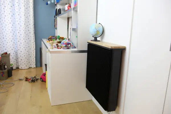 Un radiateur Qarnot particulier noir, surmonté d'un plateau en bois et d'un globe, réchauffe la chambre d'enfant remplie de jouets.