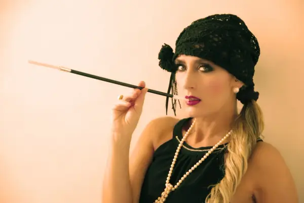 Glamurosa mujer con maquillaje de los años 20, sombrero negro y boquilla.