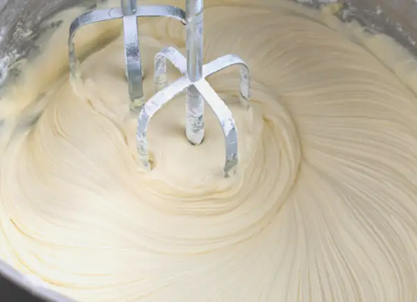 Mieszadła miksera zagłębiają się w puszysty krem z mascarpone i białej czekolady, tworząc faliste wzory.