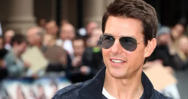 Tom Cruise w okularach przeciwsłonecznych, uśmiecha się. W tle tłum ludzi. Ciekawe, ile lat ma Tom Cruise?