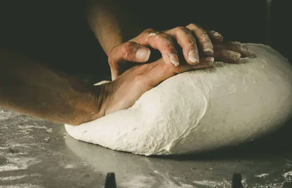 Hände kneten den Pizzateig. Die Frage "wie lange pizzateig kneten" beschäftigt jeden Bäcker.
