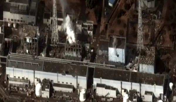 Widok z lotu ptaka na zniszczoną elektrownię Fukushima. Widać dym wydobywający się z uszkodzonych budynków, świadectwo katastrofy.