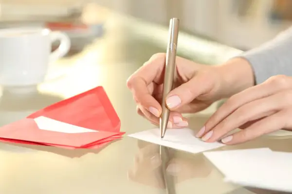 Main tenant rédige un modèle d'autorisation parentale TAM. Une tasse de café et une enveloppe rouge sont à proximité.