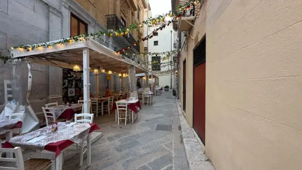 Urocza uliczka w Trapani, gdzie zjeść? Stoliki restauracyjne pod girlandami z cytryn i lampek, idealne na wieczorny posiłek.