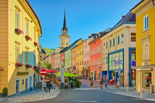 Via colorata di una città austriaca più vicina all'Italia, con edifici vivaci, una torre dell'orologio e gente che passeggia.