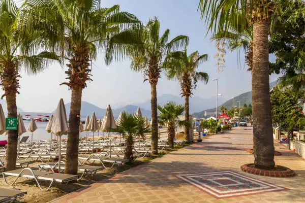 Alejka z palmami prowadzi do plaży w Marmaris, Turcja. Leżaki i parasole czekają na turystów.