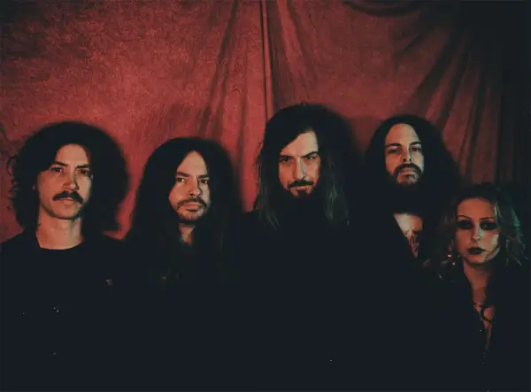 Cinq membres du groupe Uncle Acid and the Deadbeats posent devant un rideau rouge.