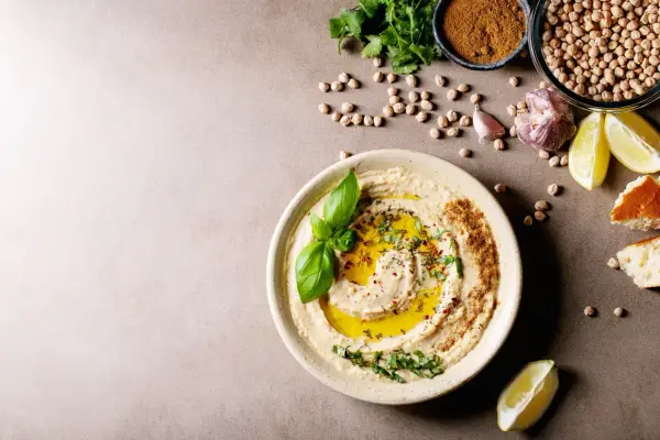 Pyszny hummus z oliwą, ziołami i bazylią. Obok ciecierzyca, czosnek, cytryna i chleb. Czy można mrozić hummus? Tak, można go mrozić.