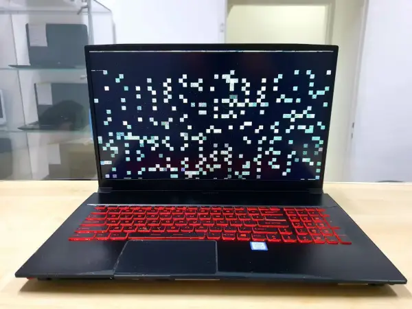 Laptop z artefaktami na ekranie, wskazującymi na problemy z kartą graficzną. Klawiatura podświetlona na czerwono.