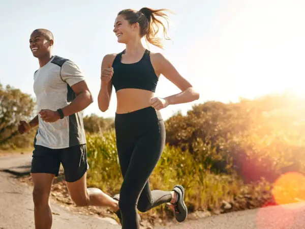 Ein Mann und eine Frau joggen lachend auf einem Feldweg. Die Sonne scheint, und die Atmung beim Joggen ist gleichmäßig und tief.