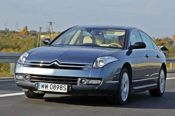 Elegancki Citroën C6 w kolorze granatowym jedzie po drodze. Wnętrze z jasną tapicerką i kierowcą.