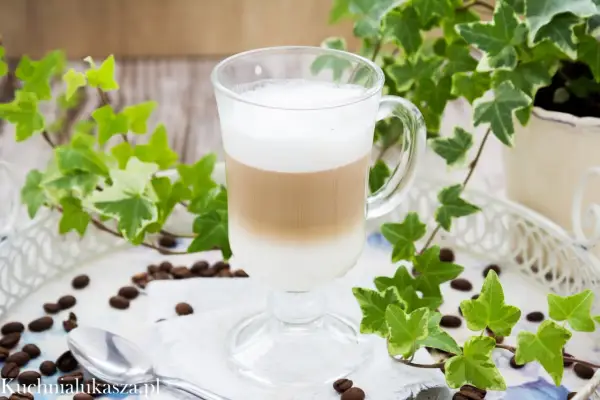 Warstwowe latte w szklance, otoczone bluszczem i ziarnami kawy. Prosty sposób, jak zrobić latte bez ekspresu.