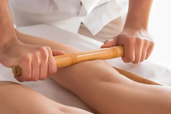 Relaksacyjny masaż pałeczkami bambusowymi na nogach. Terapeuta wykonuje głęboki masaż, przynoszący ulgę i odprężenie.