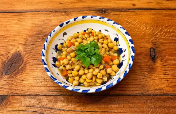 Un plat de pois chiches cuisinés avec des carottes et des oignons, garni de coriandre fraîche. La cuisson pois chiche est réussie, le plat est appétissant.