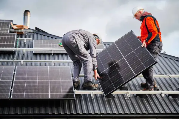 Deux ouvriers installent un panneau solaire sur un toit. La dimension du panneau solaire est adaptée pour maximiser la capture d'énergie.