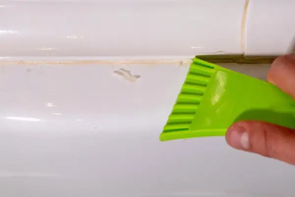 Outil vert raclant du mastic durci sur une surface blanche.