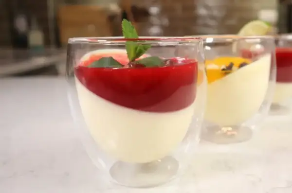 Panna cotta w szklankach z musem malinowym i miętą. Obok deser z musem mango.