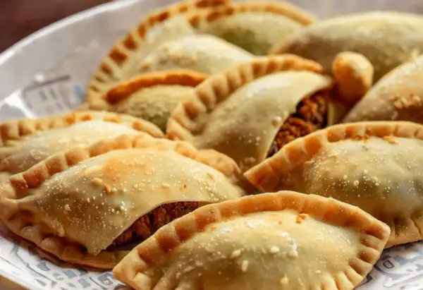 Empanadas doradas y crujientes, algunas con relleno visible de pechuga empanada, espolvoreadas con algo de sal.