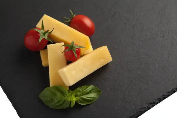 Pecorino co to? Kawałki żółtego sera, pomidorki koktajlowe i listki bazylii na ciemnej desce.
