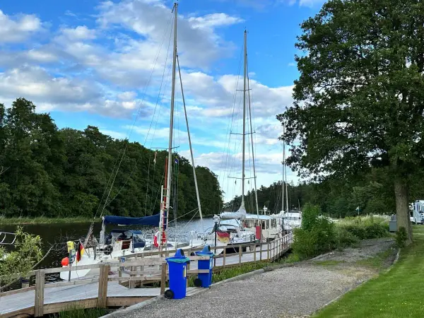 Segelbåtar vid kajen på Dalbergså camping. Grönskande träd och en blå himmel med moln.