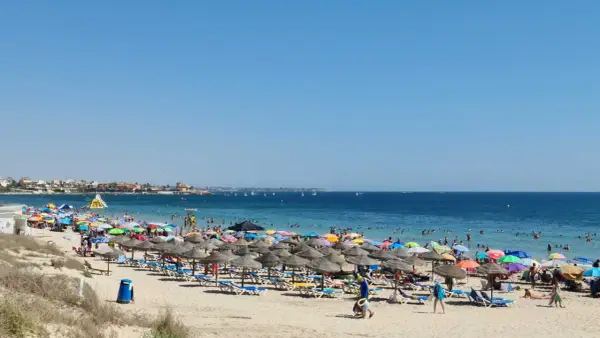 Día soleado en la playa de las Higuericas, con mucha gente disfrutando del mar y la arena bajo coloridas sombrillas.