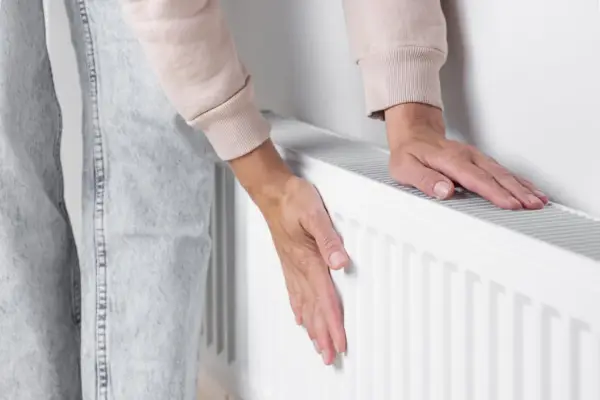 Dłonie sprawdzają temperaturę grzejnika, który słabo grzeje. Zimno w domu, trzeba coś z tym zrobić.