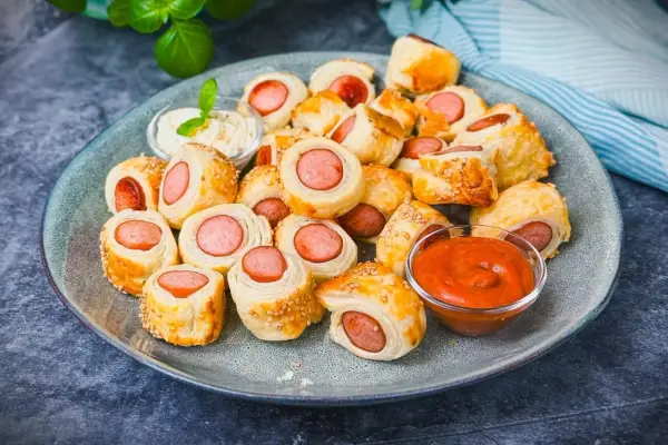 Leckeres Fingerfood für den Sommer: Würstchen im Blätterteig mit Sesam, serviert mit Dip und Ketchup.