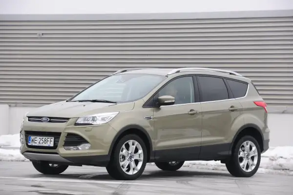 Złoty Ford Kuga 2.0 TDCI z polskimi tablicami WE 258FF zaparkowany na tle industrialnej ściany.