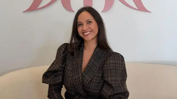 Sonriendo, una mujer con un blazer de cuadros marrones y mangas abullonadas. Sus opiniones sobre miphai son positivas.