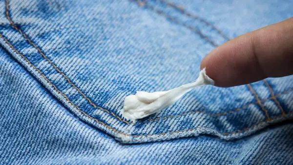 Ein Finger versucht, Kaugummi von Jeans zu entfernen. Der klebrige Kaugummi zieht sich zäh.