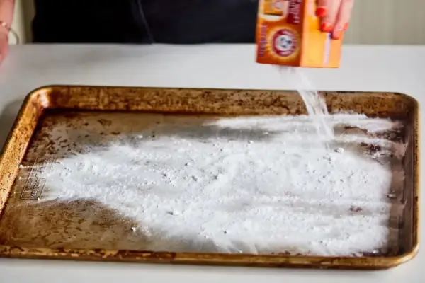 Saupoudrer du bicarbonate de soude sur une plaque de four brûlée. Une astuce pour savoir comment enlever du brûlé sur une plaque de four.