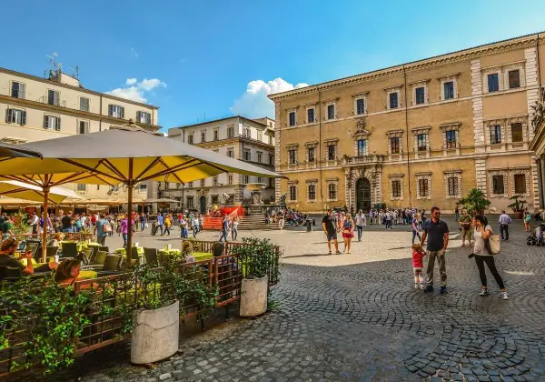 Piazza animata con gente che passeggia e si gode la movida a Roma, tavolini all'aperto e palazzi storici sullo sfondo.