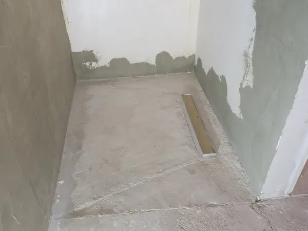 Niedawno położony szlam mineralny w łazience, z widocznym odpływem liniowym. Ściany w trakcie tynkowania.