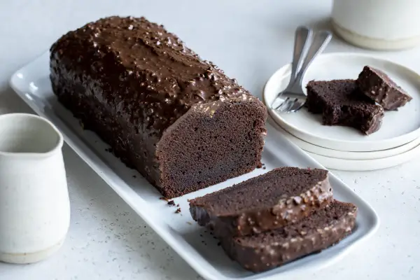 Un généreux gâteau au chocolat haut, nappé d'un glaçage croquant et parsemé de noisettes. Deux tranches sont déjà coupées, prêtes à être dégustées.