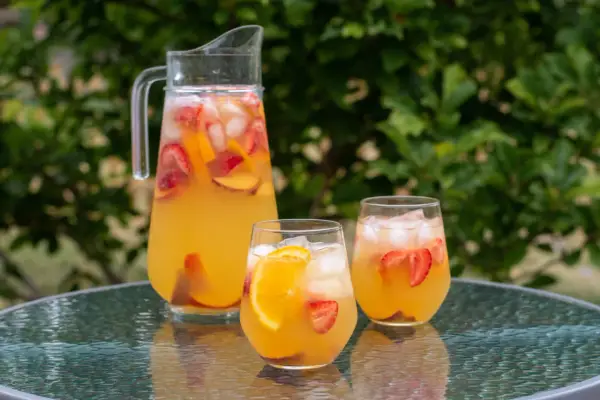 En karaff och två glas med en uppfriskande cava drink fylld med is, jordgubbar och apelsinskivor. Perfekt för en sommardag.