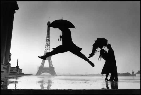 Opera d'arte di Henri Cartier-Bresson: silhouette di un ballerino con ombrello salta davanti alla Torre Eiffel, mentre una coppia si abbraccia sotto un altro ombrello.