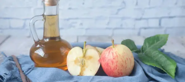 Ein Glas Apfelessig steht neben frischen Äpfeln und Blättern. Perfekt, um essig selber machen.