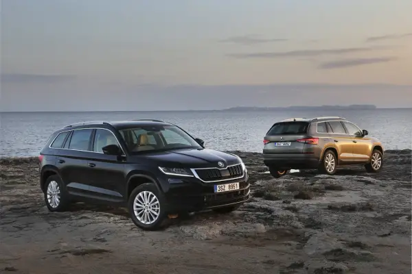 Dwa SUV-y Skoda Kodiaq 2024 na skalistym wybrzeżu. Jeden czarny, drugi w kolorze złota.