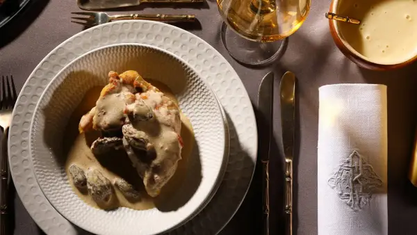 Un plat de poulet au vin jaune, crémeux et garni de morilles, servi sur une assiette texturée. Une table dressée avec élégance.